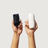 two male hands holding black colored Leo vibrating stroker and white colored Adam manual stroker from Thirdbase held against a white background